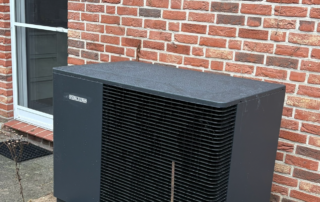 Wärmepumpe steht vor einer Backsteinhauswand.